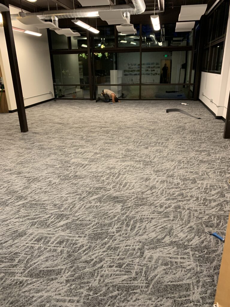 Gray carpet being installed in a large office. 